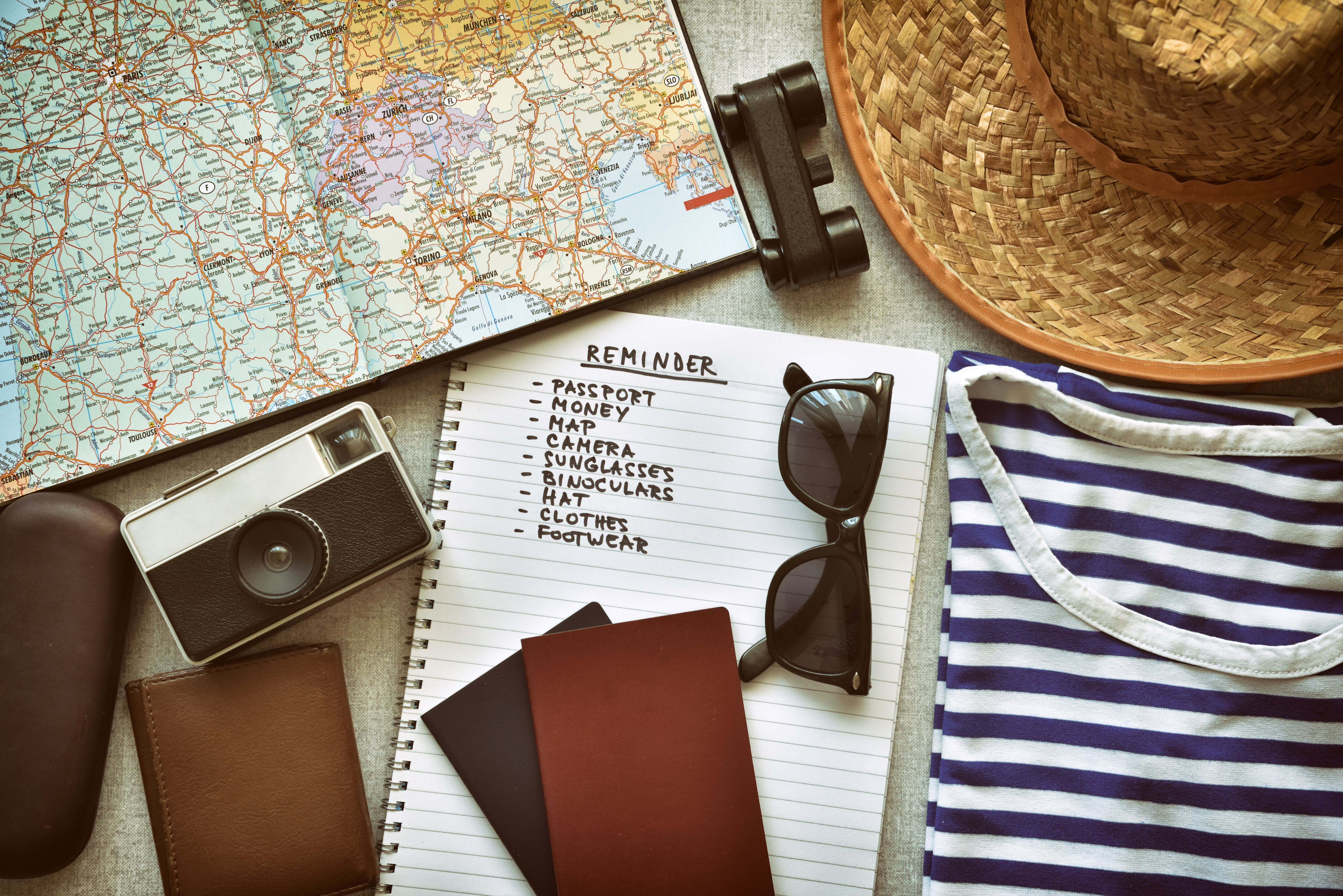 A cruise packing list featuring a passport, wallet, vintage camera, binoculars, hat, sunglasses, and a striped shirt on a map background.