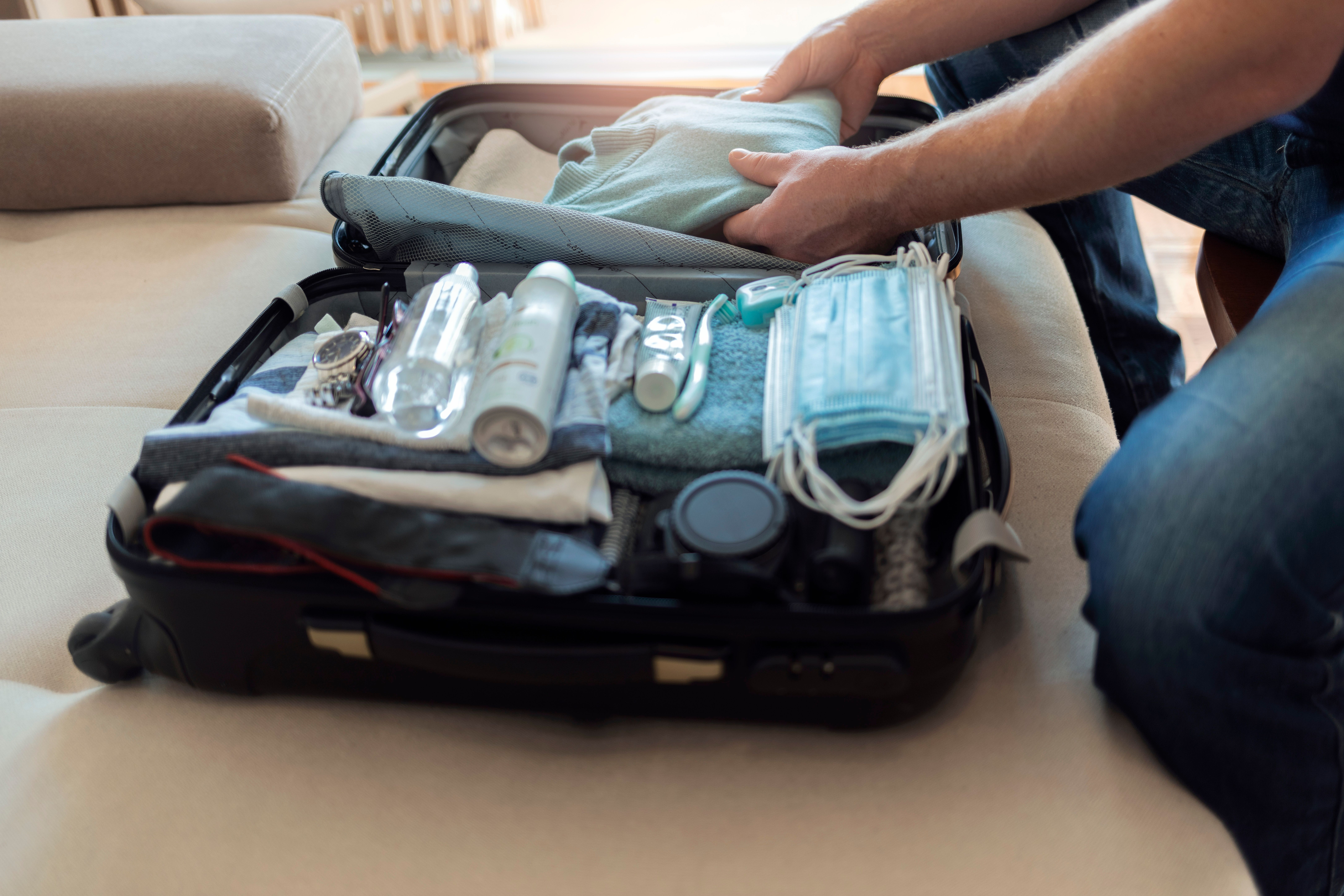 Person packing a suitcase with clothes, toiletries, a camera, and face masks, getting ready for a week-long cruise.